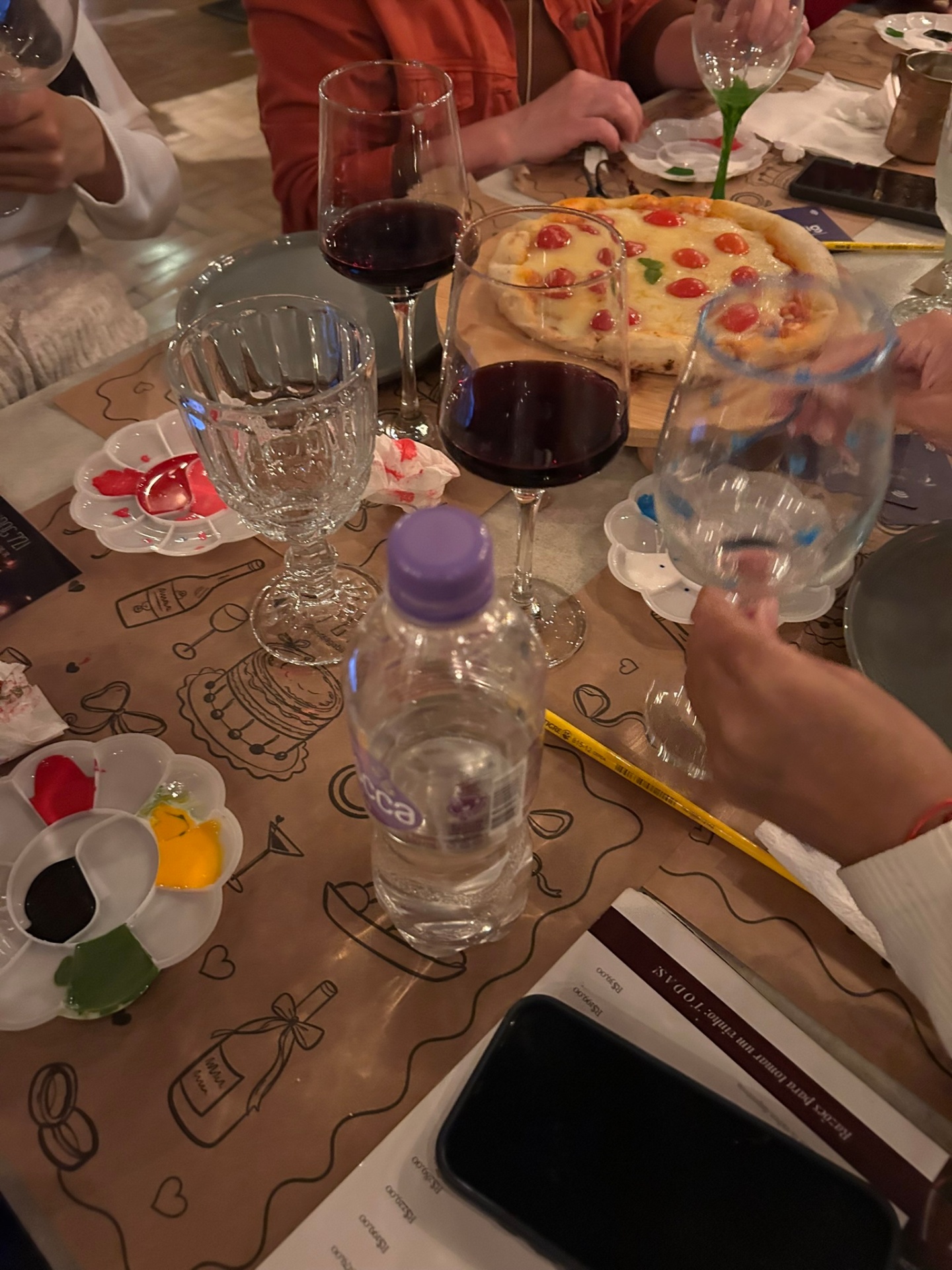 Mesa com pizza, vinho e materiais de pintura compartilhados