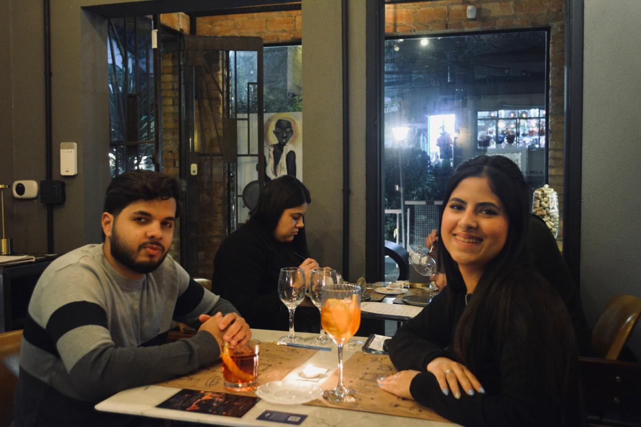 Casal sorrindo durante encontro Modo Avião com drinks na mesa