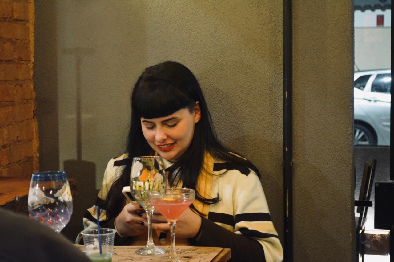 Participante sorrindo com taça pintada à mão e drink rosé